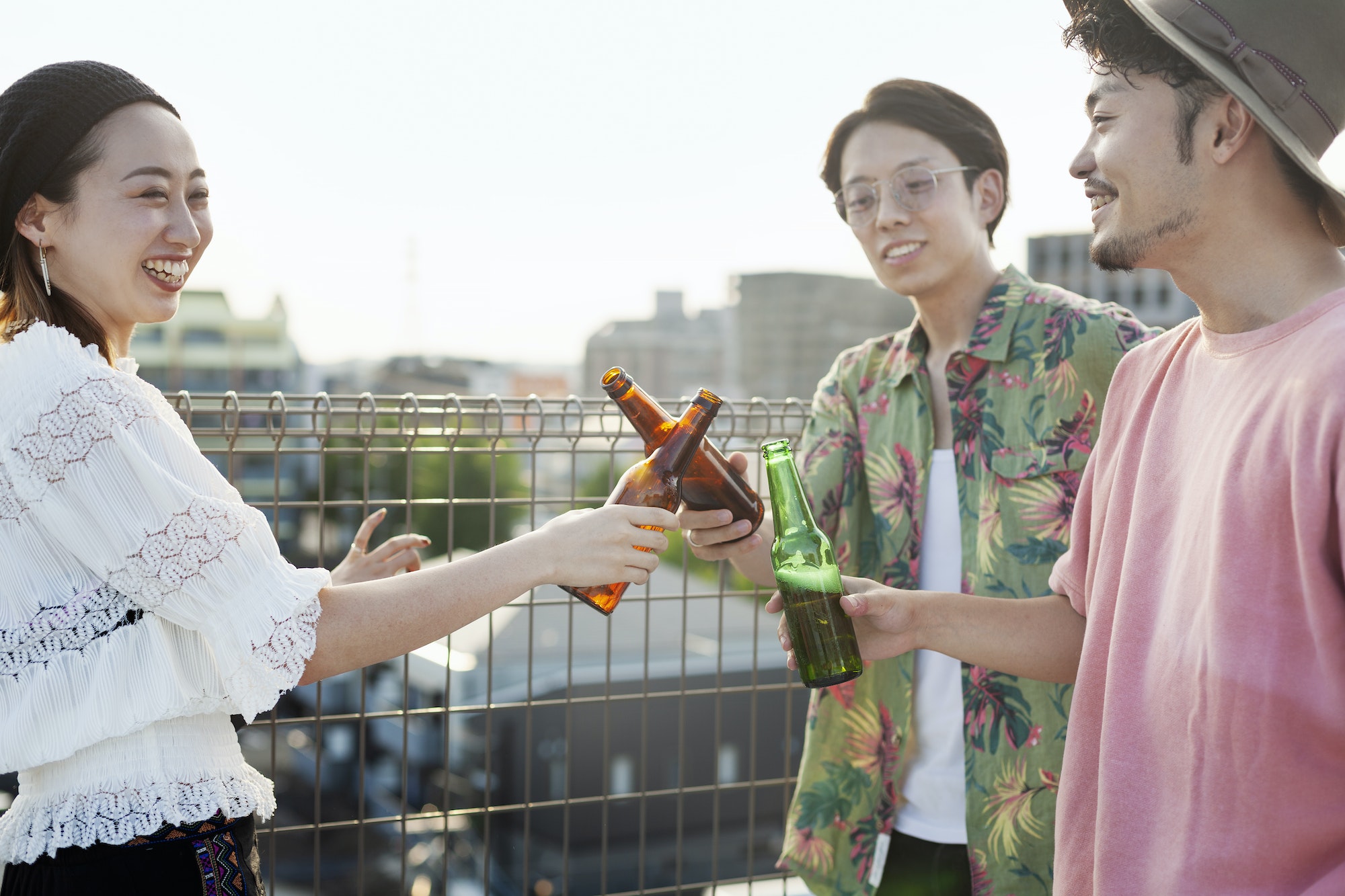 Young Japanese men and woman standing on a rooftop in an urban setting, drinking beer.